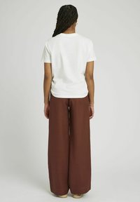 T-shirt en coton blanc associé à un pantalon ample en lin marron ; les deux pièces ont un minimum de détails et une coupe décontractée, conçues pour le confort.