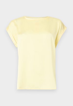 Camicia gialla chiara a maniche corte con scollo tondo e polsini leggermente arrotolati su sfondo chiaro.