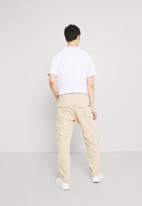 Beige cargobroek met meerdere zijzakken, elastische tailleband en taps toelopend ontwerp. Gecombineerd met een eenvoudig wit t-shirt en witte sneakers.