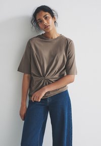 Brown knotted t-shirt with short sleeves paired with wide-leg blue denim jeans. Smooth fabric with a relaxed fit and simple design.