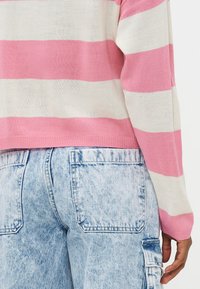 Maglione a righe con linee orizzontali rosa e bianche, realizzato in un morbido tessuto a maglia, abbinato a pantaloni cargo in denim azzurro chiaro a vita alta.