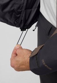 Zwarte waterdichte jas met elastisch trekkoord en toggles aan de onderkant, met een gestructureerde mouw en een label van stof met de tekst "TEXAPORE."