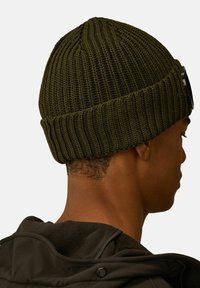 Berretto lavorato a maglia verde oliva con texture a coste e orlo piegato. Presenta un accento circolare liscio sul lato.