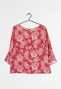 Top floreale rosso con maniche lunghe a campana, caratterizzato da un collo rotondo e un tessuto morbido e strutturato. Il design include intricati motivi floreali bianchi.