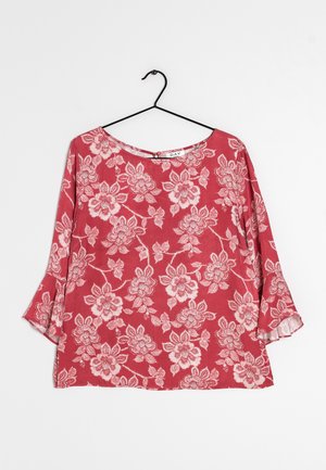 Top floreale rosso con maniche lunghe a campana, caratterizzato da un collo rotondo e un tessuto morbido e strutturato. Il design include intricati motivi floreali bianchi.