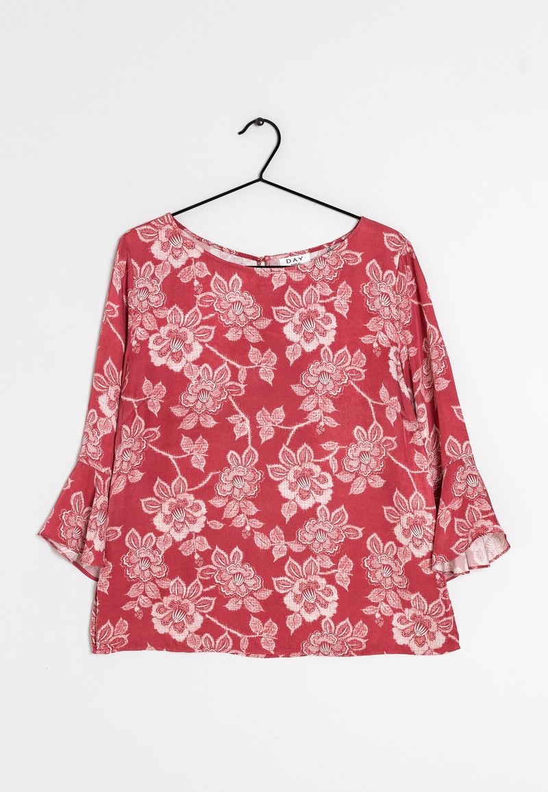 Top floreale rosso con maniche lunghe a campana, caratterizzato da un collo rotondo e un tessuto morbido e strutturato. Il design include intricati motivi floreali bianchi.