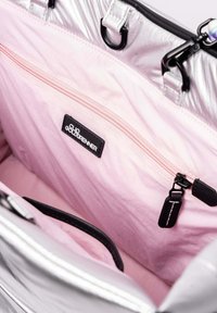 Sac fourre-tout en métal argenté doublé de tissu rose clair. Comprend une poche zippée noire avec logo, des poignées noires et un matériel contrastant.
