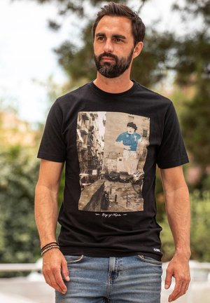 Zwarte crew-neck t-shirt met een grote geprinte foto van een kind in een blauwe trui, met de tekst "King of Naples" onder de afbeelding.