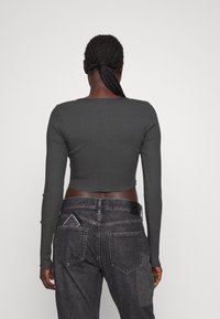 Mörkgrå kortärmad långärmad topp med ribbad textur, parat med högmidjade svarta denimjeans med bakfickor och en blekt design.