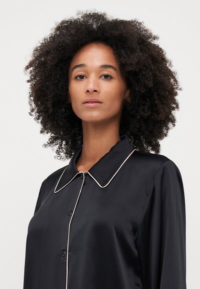 Black satin shirt with a structured collar, featuring contrasting light-colored piping along the edges and button closure on the front.