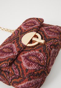 Tekstuuriga käekott lillemustriga, sügavas punases, oranžis ja roosas, millel on kuldne ümmargune lukk ja ketitaoline rihm.