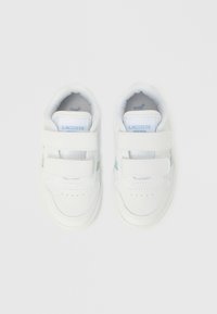 Valkoiset tarrakiinnitteiset tennarit, joissa on sileä nahkamateriaali, pyöreä kärki ja hillityt vihreät yksityiskohdat sivulla.