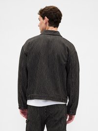 Homem de costas, vestindo um fato risca de giz preto com calças a condizer e uma camisa branca a espreitar por baixo.