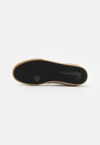 Sola de sneaker preta em borracha com um padrão em zigzag, apresentando um detalhe central em forma de estrela, rodeado por uma borda bege.