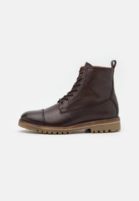 Bruna läderankelstövlar med texturerad finish, rund tå och snörningsdesign. Tjock gummisula med framträdande mönster och en dragflik på hälen.