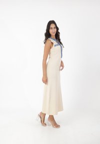 Lang, cremet ribbet kjole med en denim knapp-up overdel og en udvidet silhuet. Båret med klare blokhælsandaler. Glat tekstur.