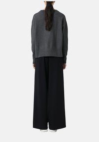 Grauer Strickpullover mit lässiger Passform, ausgestattet mit einem gerippten Saum. Kombiniert mit weiten schwarzen Hosen, die eine glatte Textur haben.