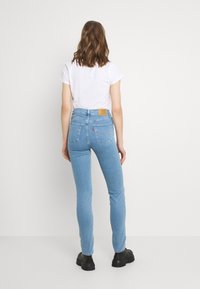 Jeans de tiro alto en azul claro con un corte ajustado, que cuentan con dos bolsillos traseros, costuras sutiles y un parche de marca de cuero en la cintura.