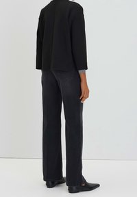 Svart kort sweatshirt med rak skärning på baksidan, matchad med mörka jeans. Slim fit, med en subtil textur och klassiska fickor.