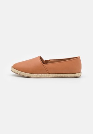 Tan slip-on sko med flad sål indhyllet i jute, glat læderoverdel og elastisk sidepanel for nem påtagning.