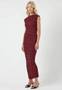 Burgunderfarget kjole med tettsittende silhuett og teksturerte blomsterapplikasjoner. Kappelignende ermer og en knelengde design fremhever helhetsformen.