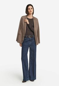 Brun kavaj över mörk topp, kombinerad med vida blå jeans. Skorna är mörkbruna med en slät textur. Enkel design, neutral färgpalett.