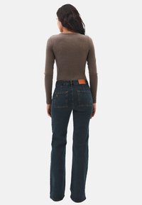 Jeans acampanados de mezclilla oscura con una cintura alta, que cuentan con dos bolsillos traseros y un parche de cuero marrón en la cintura. Combinados con una blusa de manga larga con canalé.