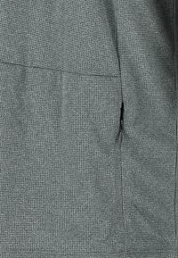 Grå texturerad tyg med ett våffelmönster, med en sidoficka med dragkedja och en slät finish vid sömmarna, som erbjuder en andningsbar och lätt design.