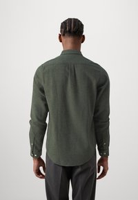 Long-sleeve shirt in dark green, made from textured fabric. Features a tailored collar and buttoned cuffs, with a curved hemline.