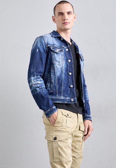Spijkerjack in verschillende tinten blauw met knoopsluitingen, borstzakken en verfspatten. Gecombineerd met beige cargobroek.