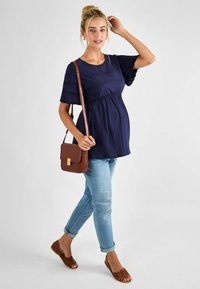 Kék navy kismama felső rövid, fodros ujjakkal és rugalmas derékkal, világoskék farmerrel és barna keresztpántos táskával kombinálva. Szőtt barna szandál.