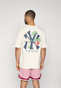 Cream-colored t-shirt featuring a large navy blue New York Yankees logo, with floral accents including a strawberry and pink flowers.