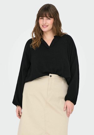 Blouse noire à manches longues avec un décolleté en V, coupe ample et tissu texturé, associée à une jupe haute beige clair à taille haute avec un bouton sur le devant.