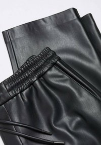 Pantalon noir en similicuir avec taille élastique et cordon de serrage, présenté plié sur fond blanc.