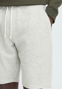 Pantalones cortos de color gris claro hechos de una suave mezcla de algodón, con una cinturilla elástica y cordones blancos, además de bolsillos laterales.