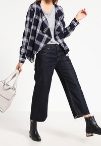 Marinblå och vit rutig kavaj över en grå T-shirt, parat med mörka jeanscroppade byxor och svarta ankelstövlar, hållande en ljusgrå väska.