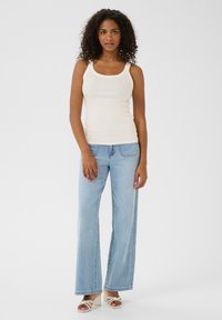Hellbeige Tanktop mit Rippstruktur und Verzierungen, kombiniert mit hellblauen weit geschnittenen Jeans. Model trägt weiße Absatzsandalen.