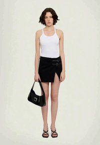 Top de tanque branco, saia mini preta com fendas laterais e dois detalhes prateados, bolsa preta e sandálias de salto alto pretas com tiras.
