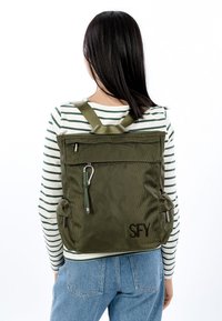 Õlivilja rohelise kangaga seljakott, millel on polsterdatud rihmad ja tekstureeritud viimistlus. Varustatud tõmblukuga katus, esist taskut ja külgseid silmuseid. Tikitud initsiaalid "SFY".