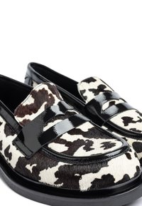 Koeienprint loafers met een zwart glanzende leren band, voorzien van een textuur die lijkt op bont, ronde neus en een zwarte rubberen zool.