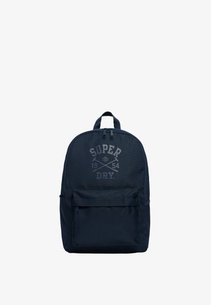 Marineblå rygsæk med lynlåslomme foran, topgreb og "Super Dry 1954"-logo trykt i gråt på hovedrummet.