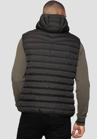 Veste sans manches matelassée noire avec motif matelassé horizontal et une capuche. Le dos présente une texture lisse et des accents côtelés à l'ourlet et aux ouvertures des bras.