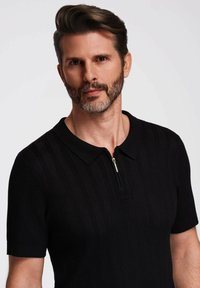 Black short-sleeve polo shirt featuring a zippered collar and textured stripe pattern. Soft fabric with a fitted design.