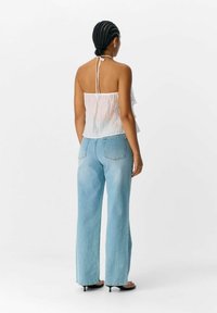 Witte, lichte haltertop met volants, gecombineerd met lichtblauwe, hoge taille wijde jeans, gezien van de achterkant.