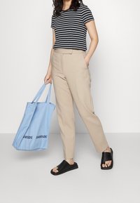 Randig svart och vit t-shirt, beige skräddarsydda byxor, svarta sandaler. Ljusblå tote-väska med "SAMSØE" tryckt i svart.