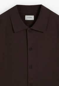 Camisa de botones marrón oscuro con cuello clásico, etiquetada "SCALPERS" talla XL, hecha de tela suave.