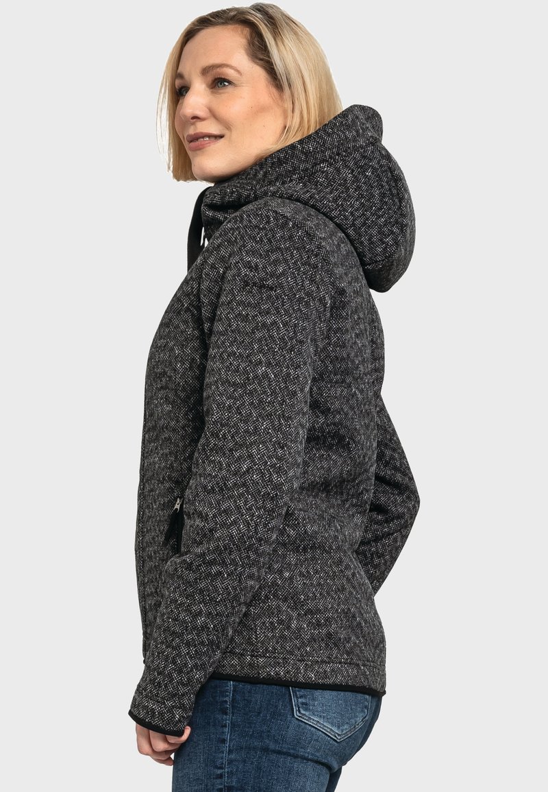 Giacca con cappuccio a motivo nero e grigio con finitura testurizzata, dotata di zip anteriore e tasche laterali, indossata con jeans blu.