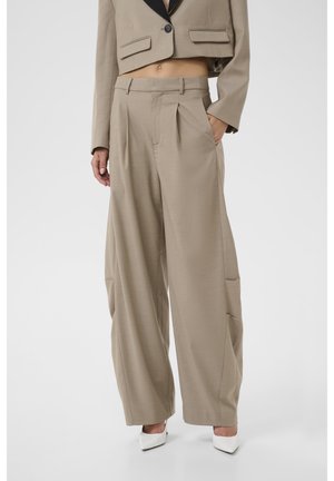 Pantalon beige à jambes larges avec plis porté avec un blazer beige court à revers noirs et talons blancs pointus.