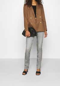 Blazer de cuadro marrón de doble botonadura, top corto negro, jeans gris ajustados y bolso de mano negro. Sandalias de tacón abiertas.