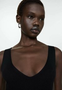 Débardeur noir à côtes avec un décolleté plongeant, des bretelles larges et une coupe cintrée. Texture lisse et style minimaliste.